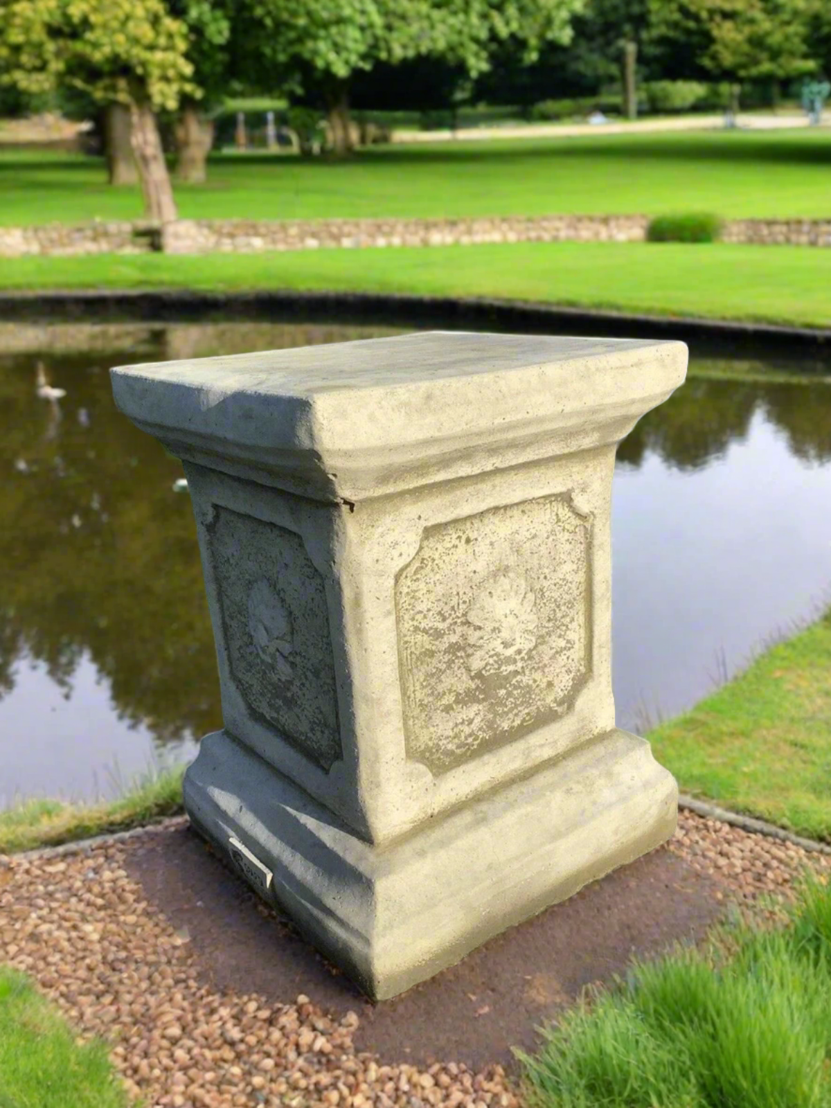 Small design stone garden plinth placed by a pond, enhancing outdoor décor with its elegant and timeless pedestal structure.