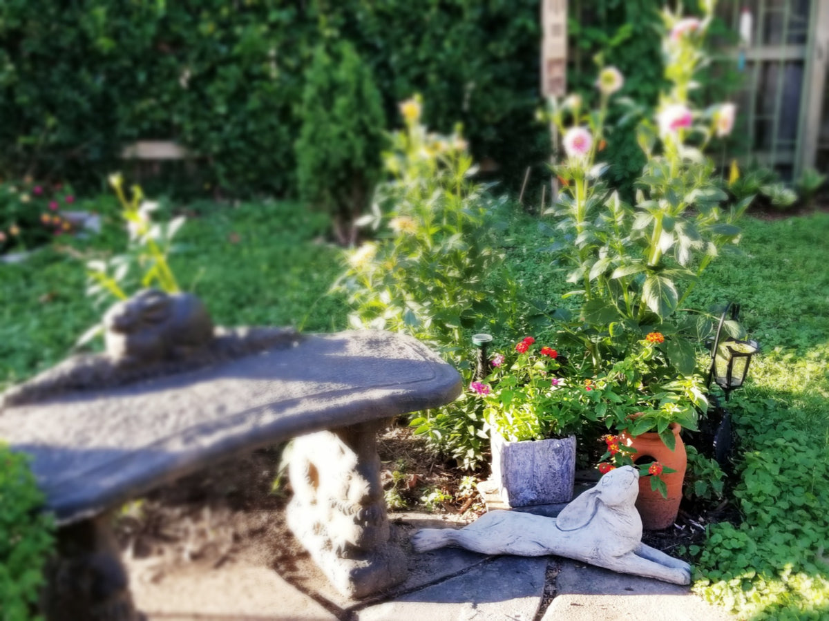 Laying Down Stone Hare Garden Ornament placed among flowers and patio decor, enhancing garden ambiance with rustic elegance.