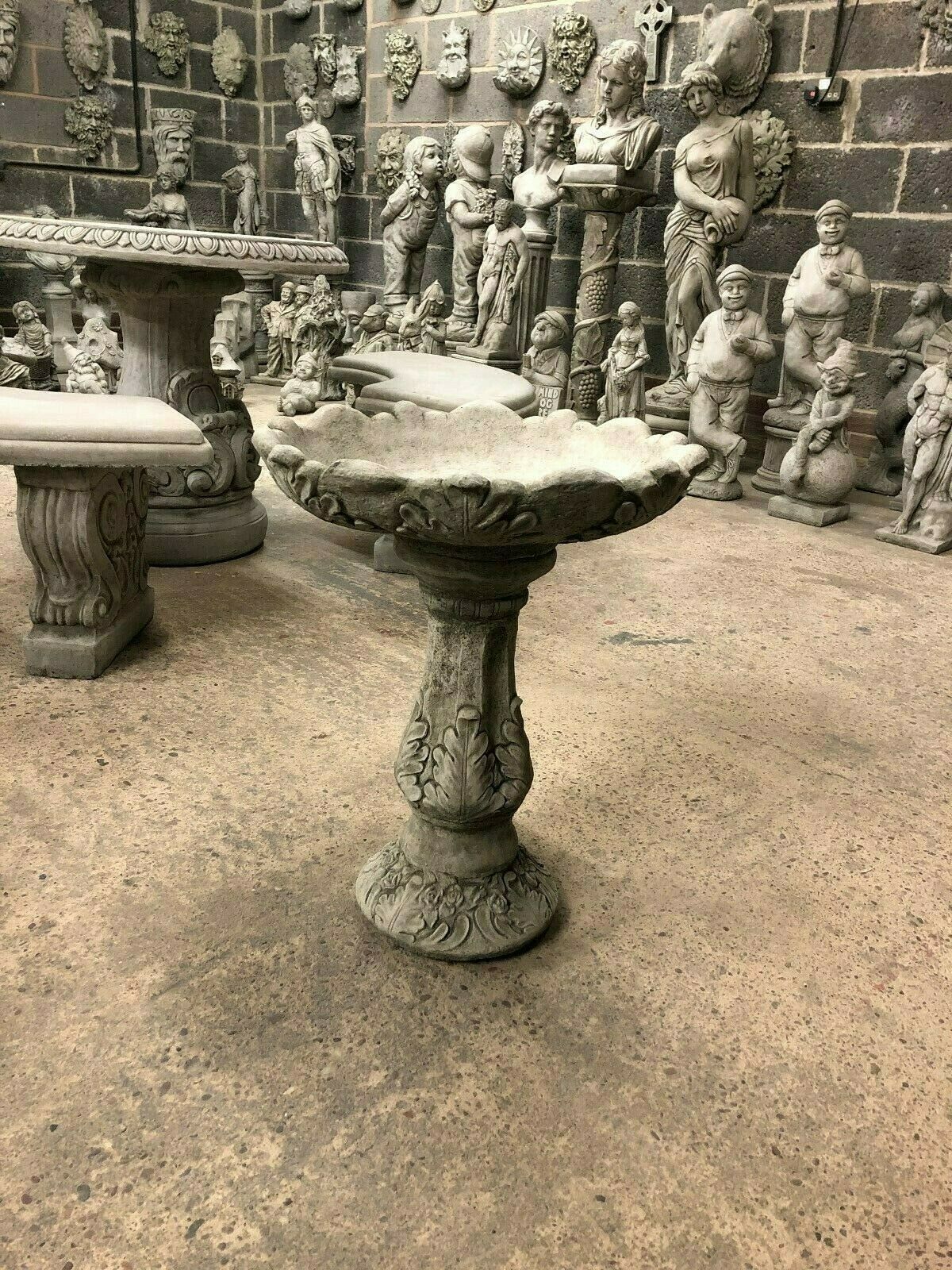 Full view of Garden Bird Bath - Leaf Design Stone in a showroom with statues, showcasing its elegant and timeless garden appeal.