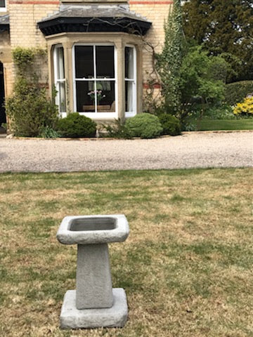 Chunky square stone bird bath in front of a classic home. Durable limestone piece adds charm and function to outdoor spaces.