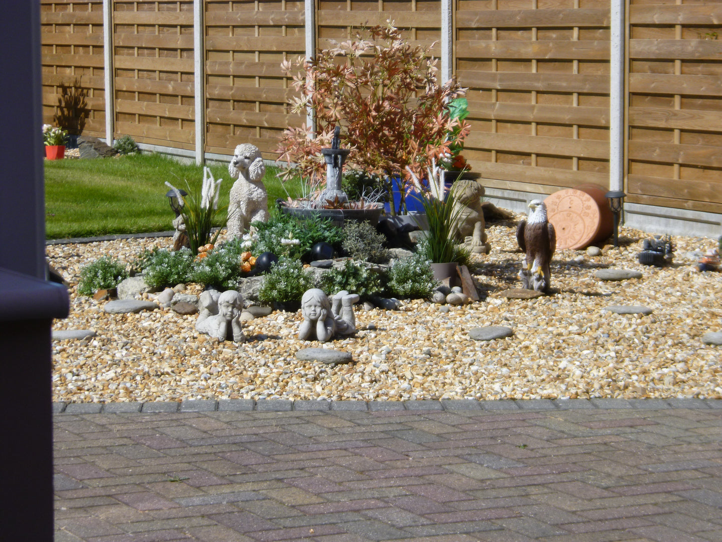 Wide view of landscaped garden with stone garden ornaments including laying boy and girl pair. Enhances outdoor decor with antique charm.