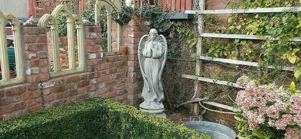 Limestone Praying Angel Garden Statue placed in a corner garden nook with trellis and flowers, ideal as a decorative outdoor lawn ornament.