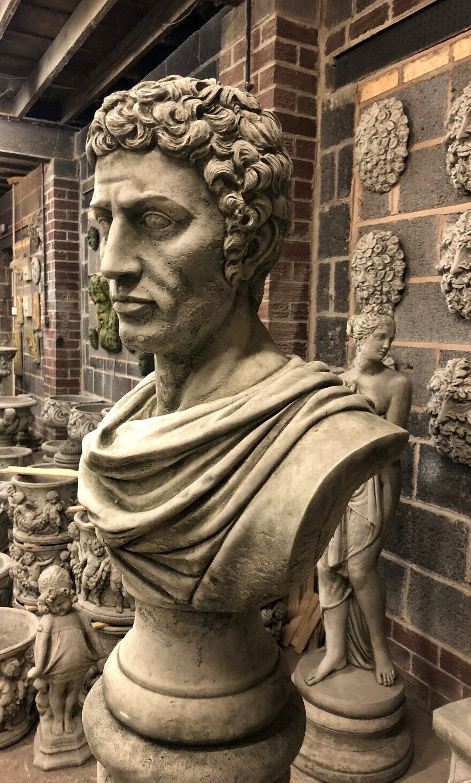 Left profile of Stone Marc Anthony Bust Statue on limestone pedestal, showcasing classical Roman design for outdoor garden ornament use.