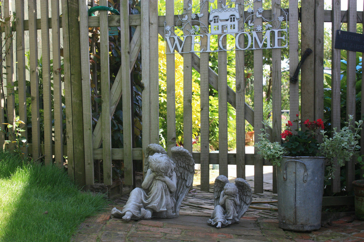 Pair of Garden Angel Statues near wooden gate with welcome sign, creating a peaceful and inviting garden entrance with antique charm.