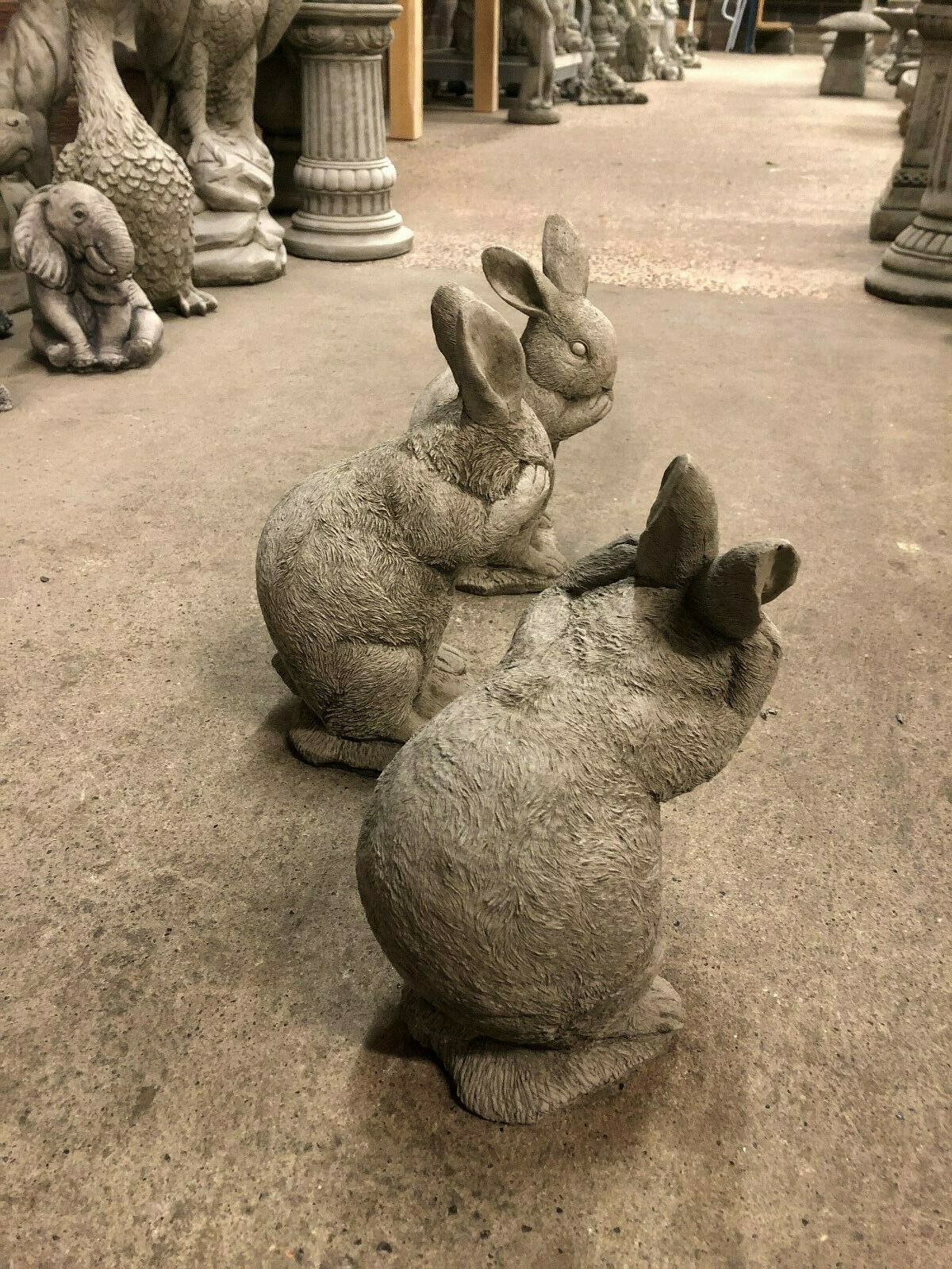 Side angle of stone Rabbit Trio garden statues showing textured detail and whimsical expressions in classic no evil poses.