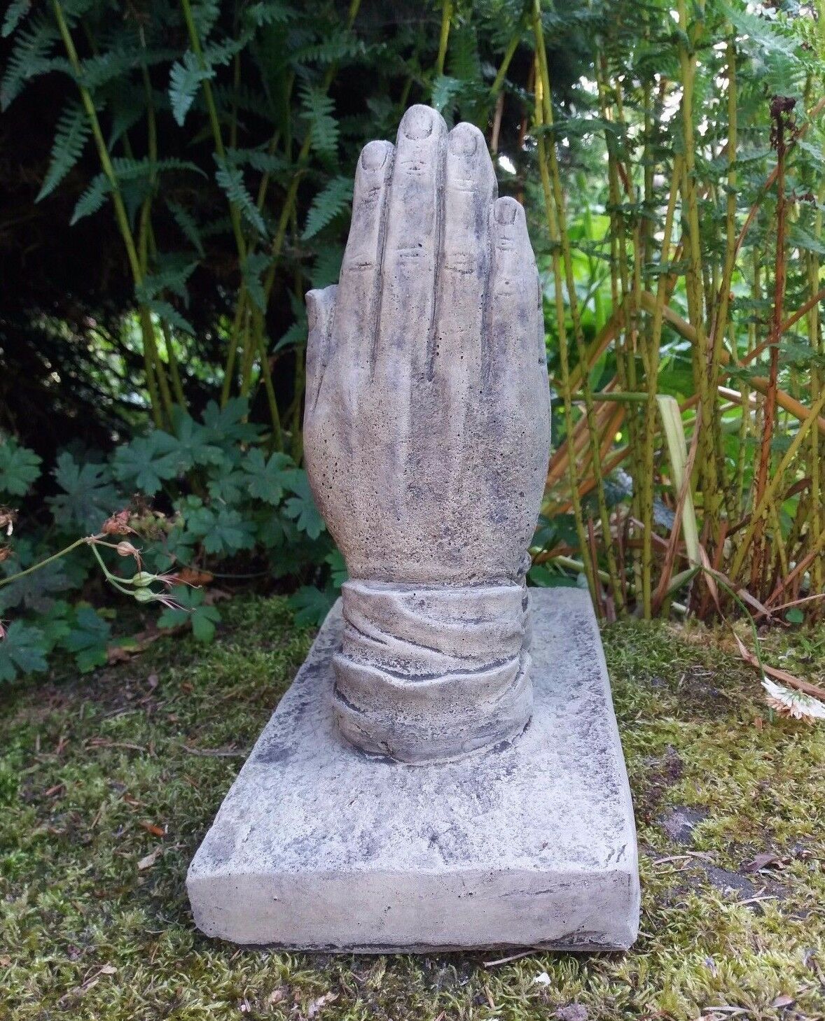 Vertical view of stone prayer hands ornament in garden setting. Memorial piece crafted from frostproof limestone with aged detailing.