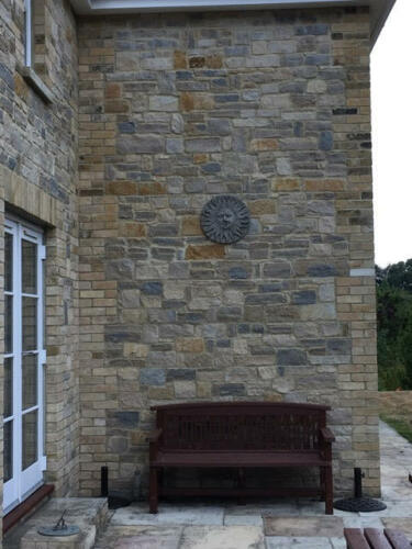 Large stone sun moon plaque displayed above a garden bench on a brick wall, enhancing patio decor.