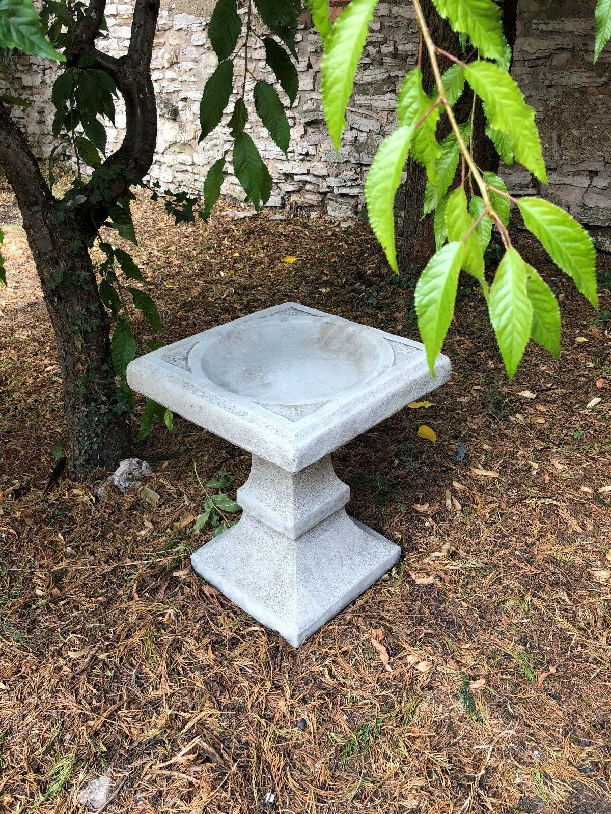 Stone Square Bird Bath nestled in a garden corner, offering a decorative and functional water source for birds in outdoor spaces.
