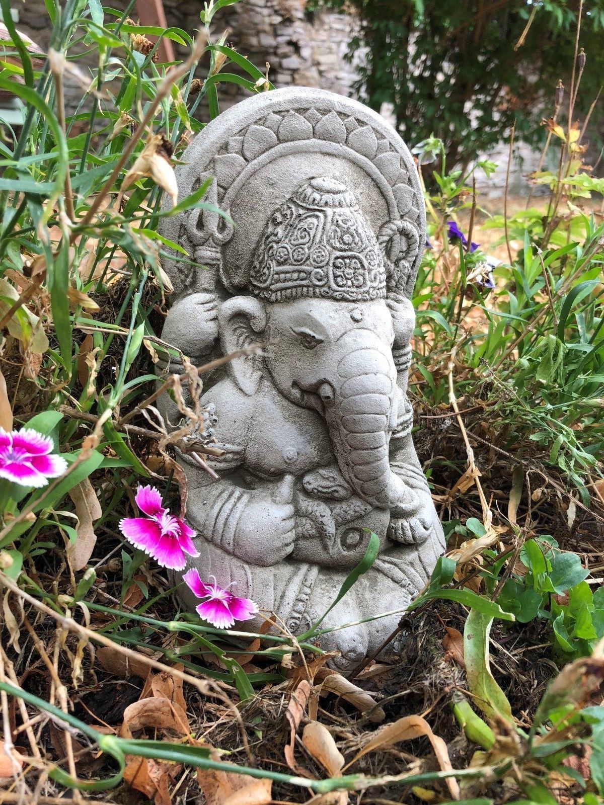 Small Stone Ganesh Garden Ornament surrounded by wildflowers. Weatherproof and detailed for spiritual garden ambiance.