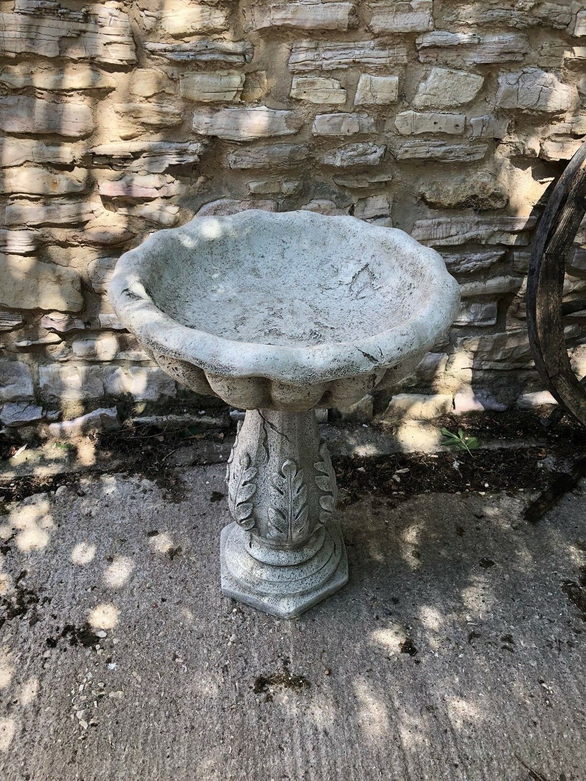 Full view of Leaf Design Garden Bird Bath with antique stone finish, placed against a textured stone wall in garden setting.