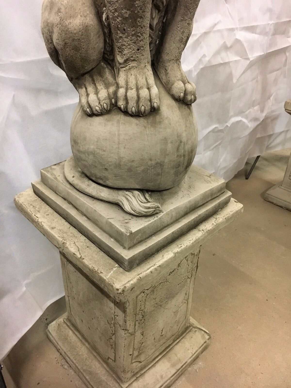 Base of a stone lion plinth statue with realistic paw and tail detailing, highlighting craftsmanship for garden or home entrance decor.