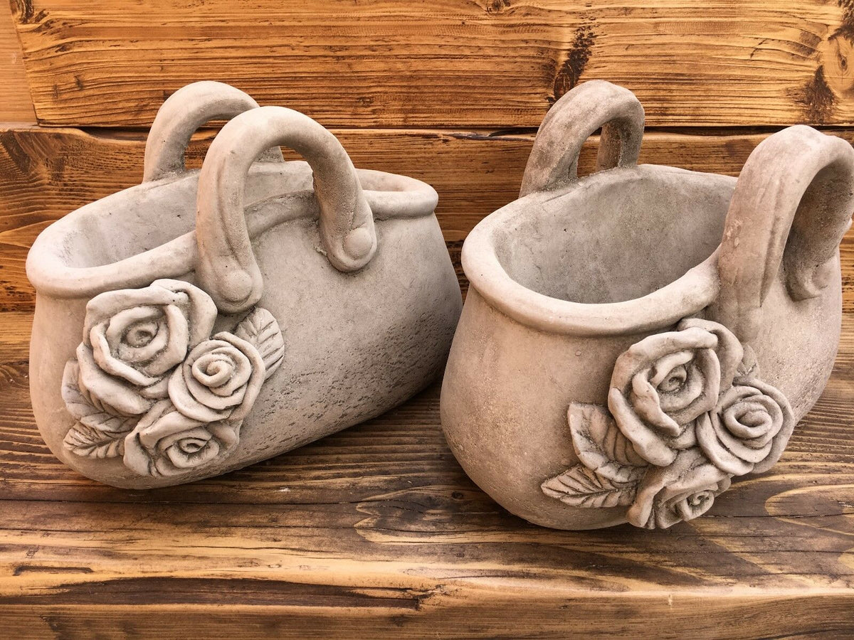 Pair of stone handbag planters with intricate rose carvings. Durable and decorative flower pots for garden or outdoor settings.