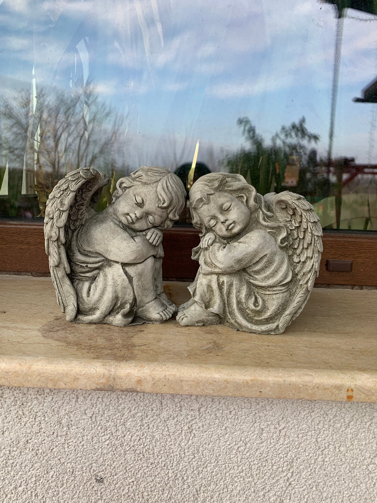 Pair of stone angel garden ornaments displayed on a windowsill. Durable limestone statues ideal for outdoor or indoor decorative use.
