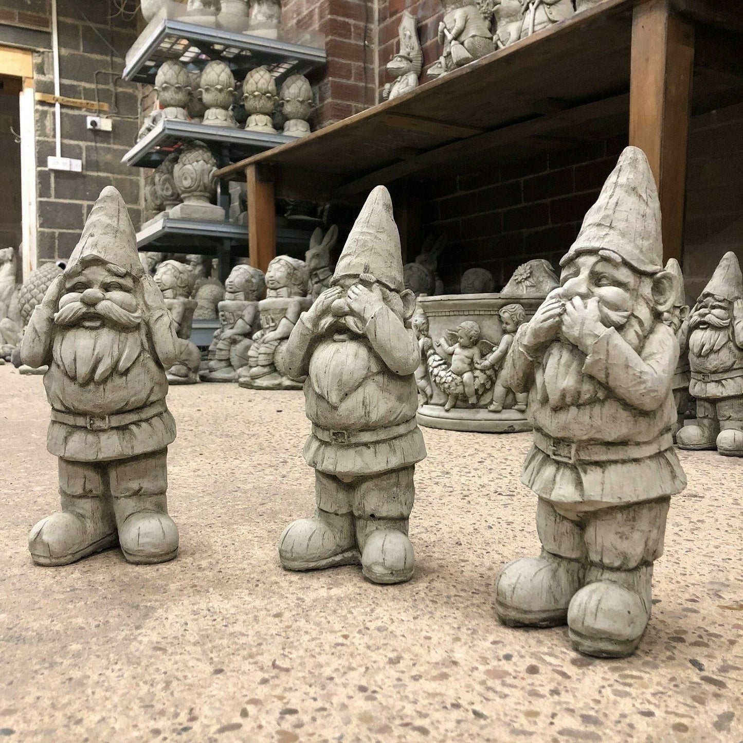 Trio of Stone Hear See Speak No Evil Gnome Statues in a workshop setting. Durable garden sculptures with antique grey finish.