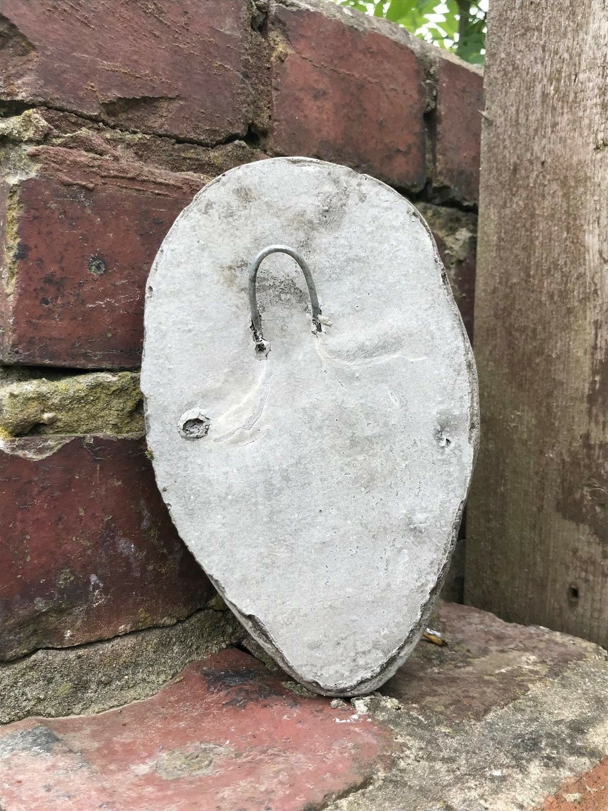 Back of the Stone Scream Face Garden Plaque featuring a metal hook for easy wall mounting, crafted from solid limestone for outdoor use.