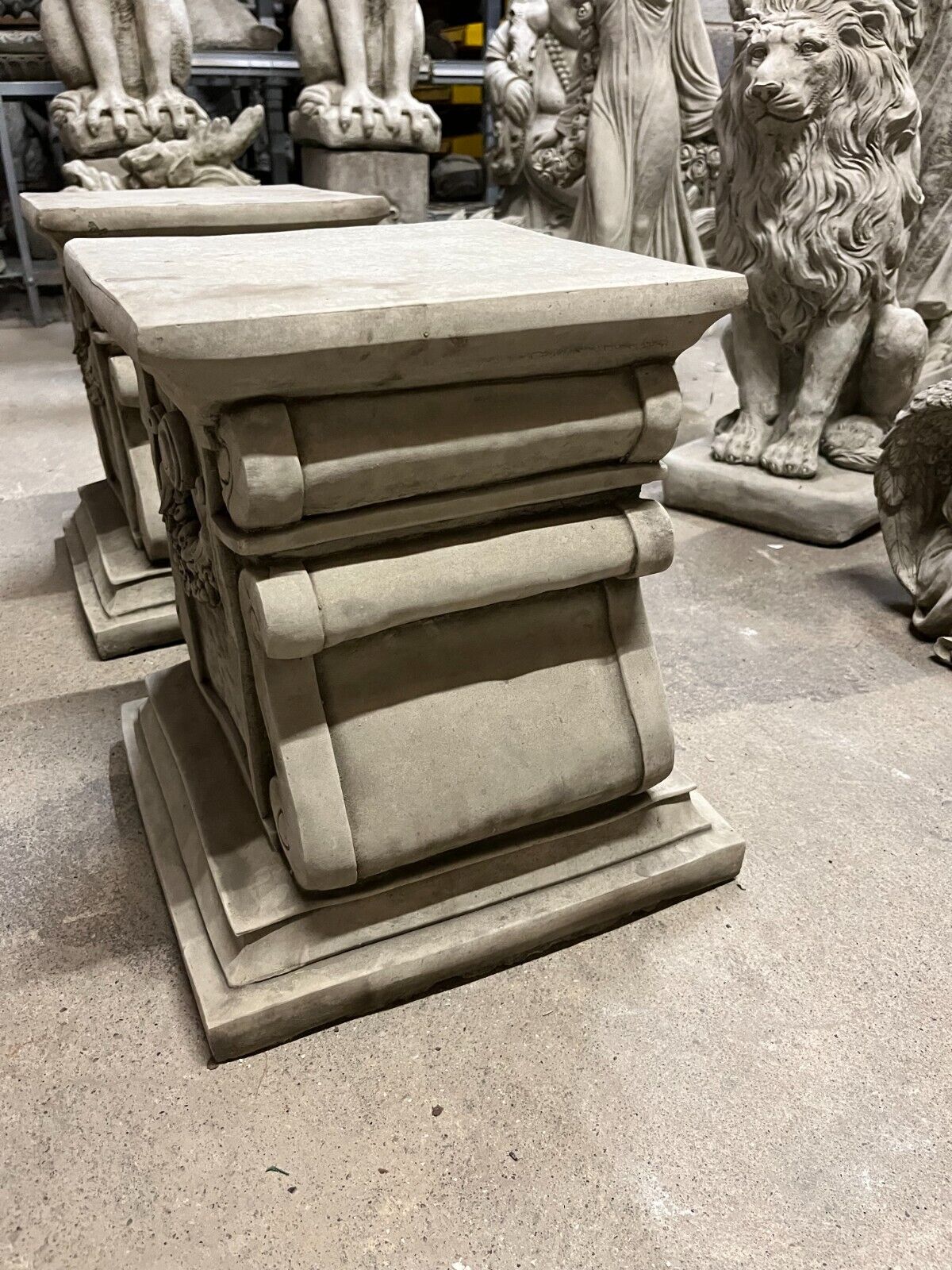 Side profile of solid stone garden plinths with classical scroll design, ideal for supporting statues or decorative urns.