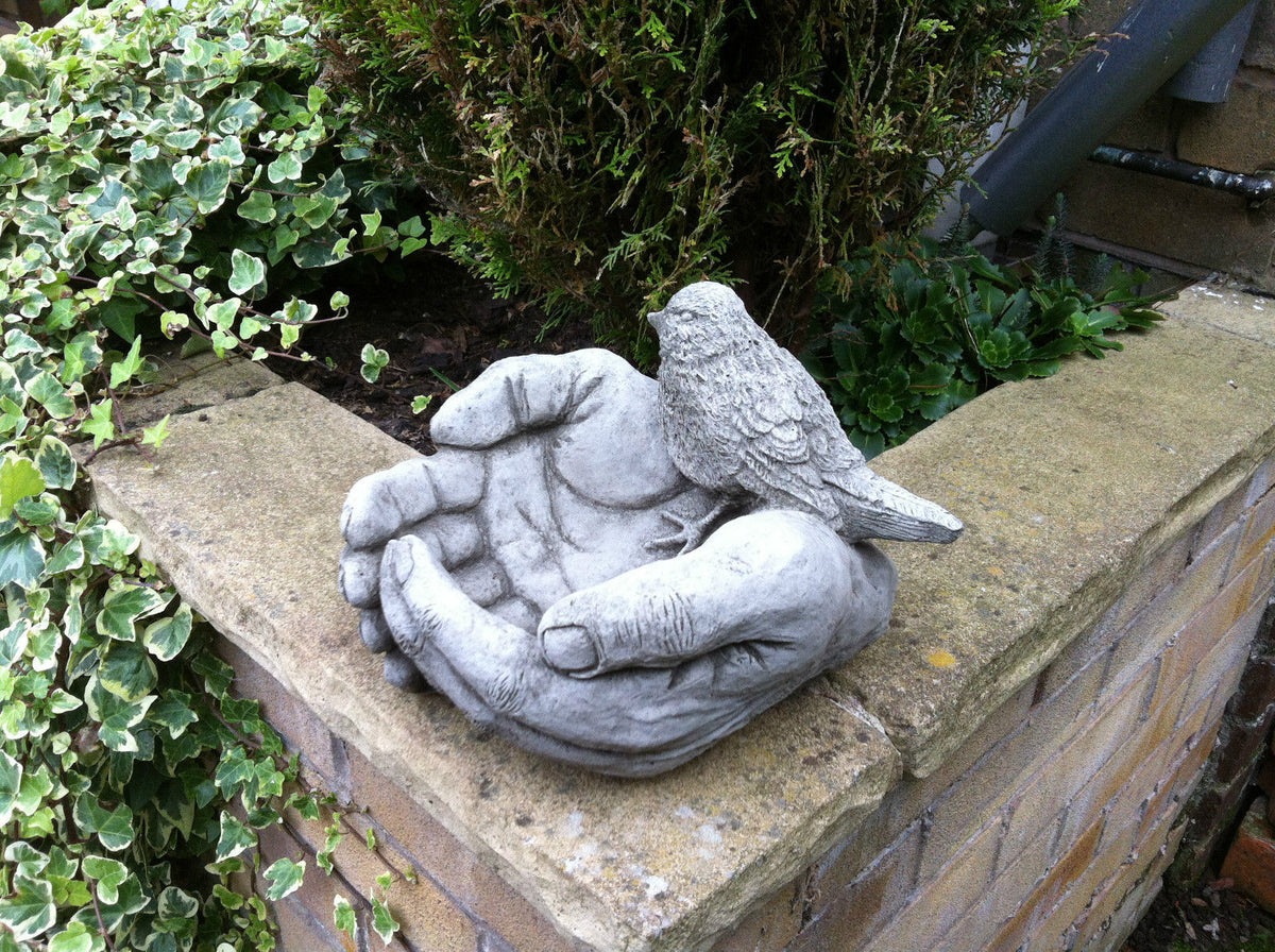 Stone Hands Design Bird Bath/Feeder with Durable Finish placed on a brick wall, showcasing realistic bird detail and weather-resistant surface.
