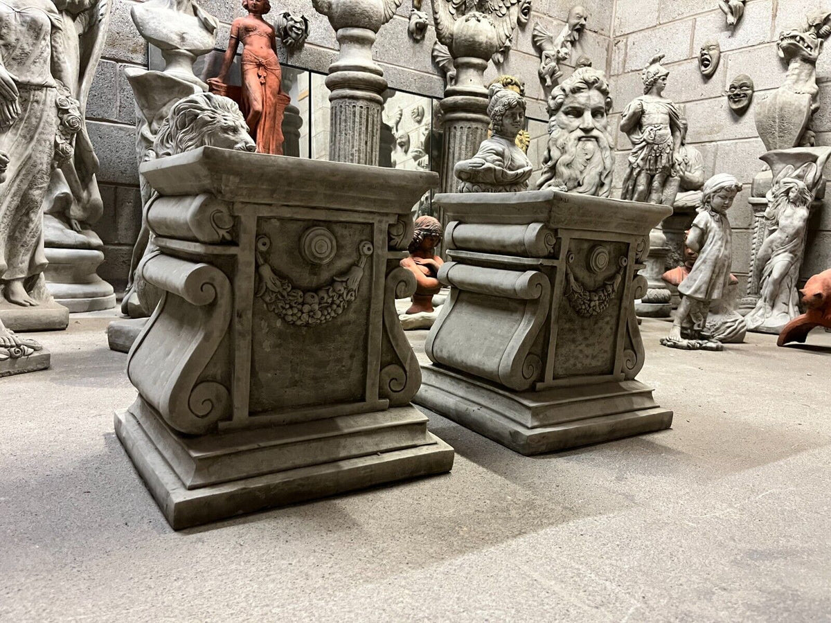 Pair of antique-style garden stone garland plinths with floral swag detail, ideal for elegant statue display in home or garden decor.