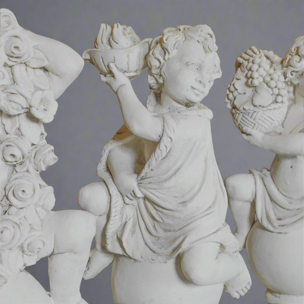 Close-up of Summer and Autumn cherub statues from the Four Seasons Stone Statues set, highlighting detailed carvings of fruit and floral elements.