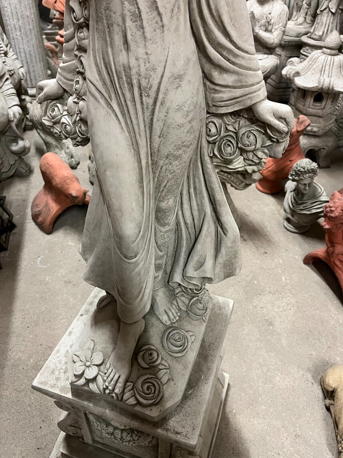 Top-down view of garden statue's base showing bare feet and detailed stone roses, emphasizing craftsmanship and design.