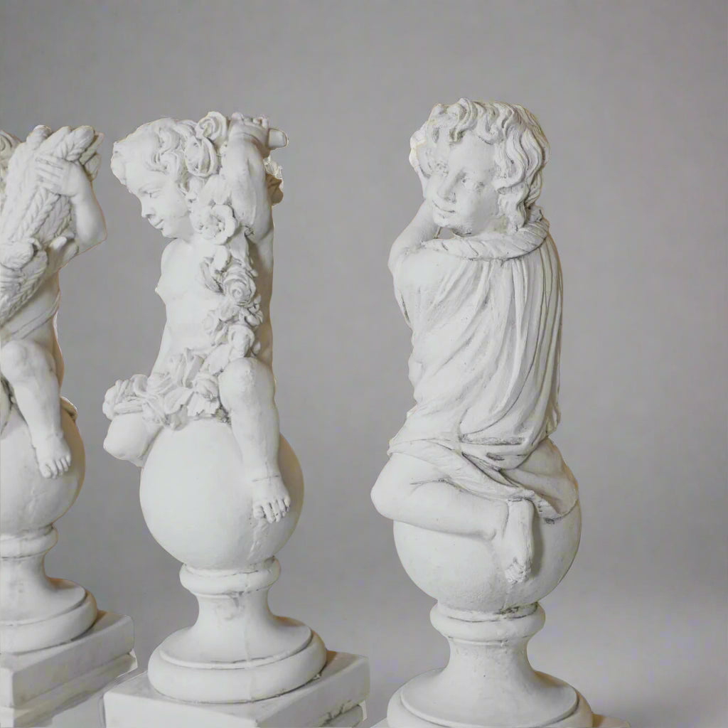 Side view of Spring and Summer cherub statues from the Four Seasons Stone Statues set, emphasizing floral garlands and seasonal symbolism.