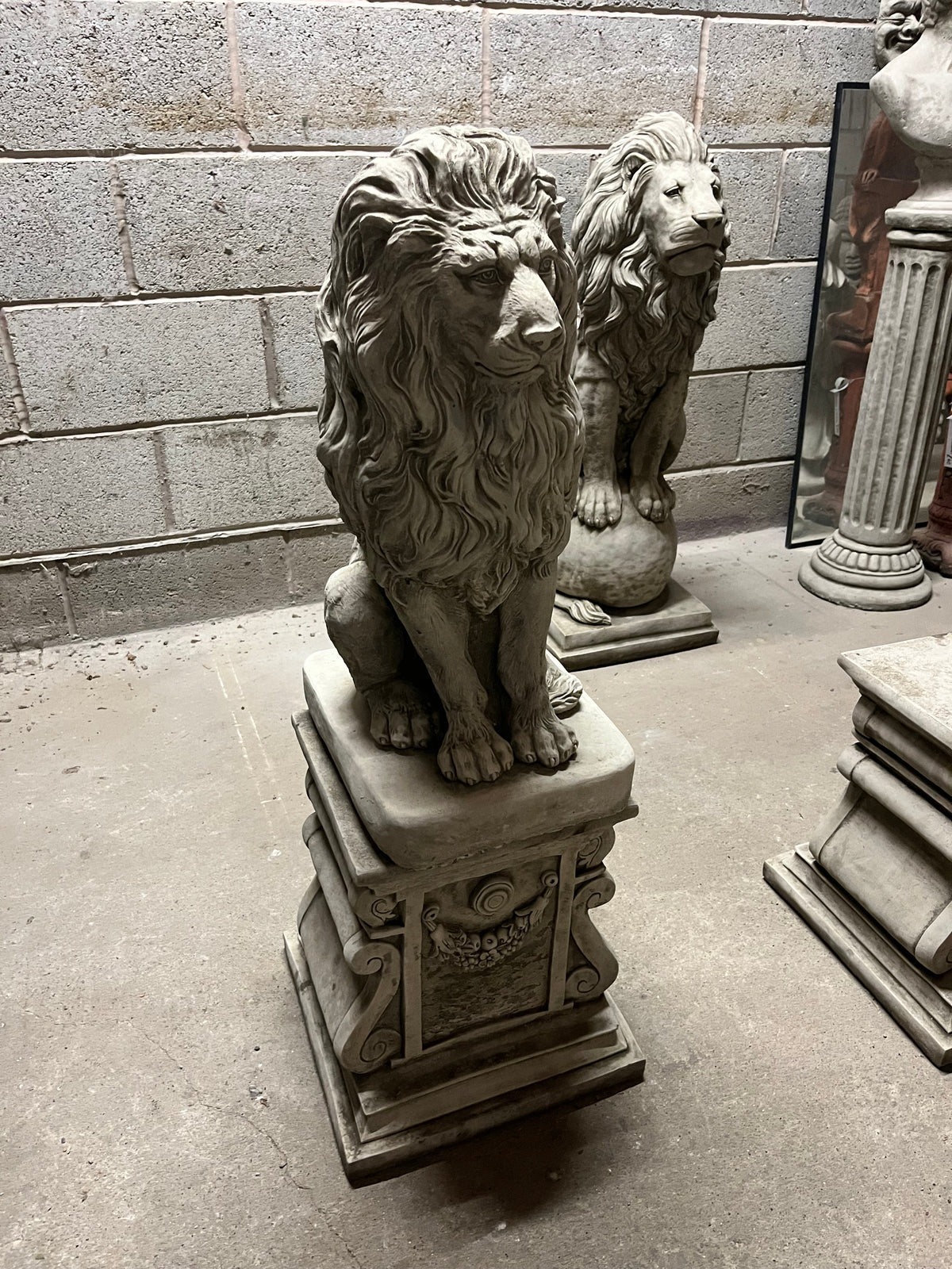 Stone lion statue on ornate plinth with floral detailing, perfect for elegant garden decor or lawn sculpture display.