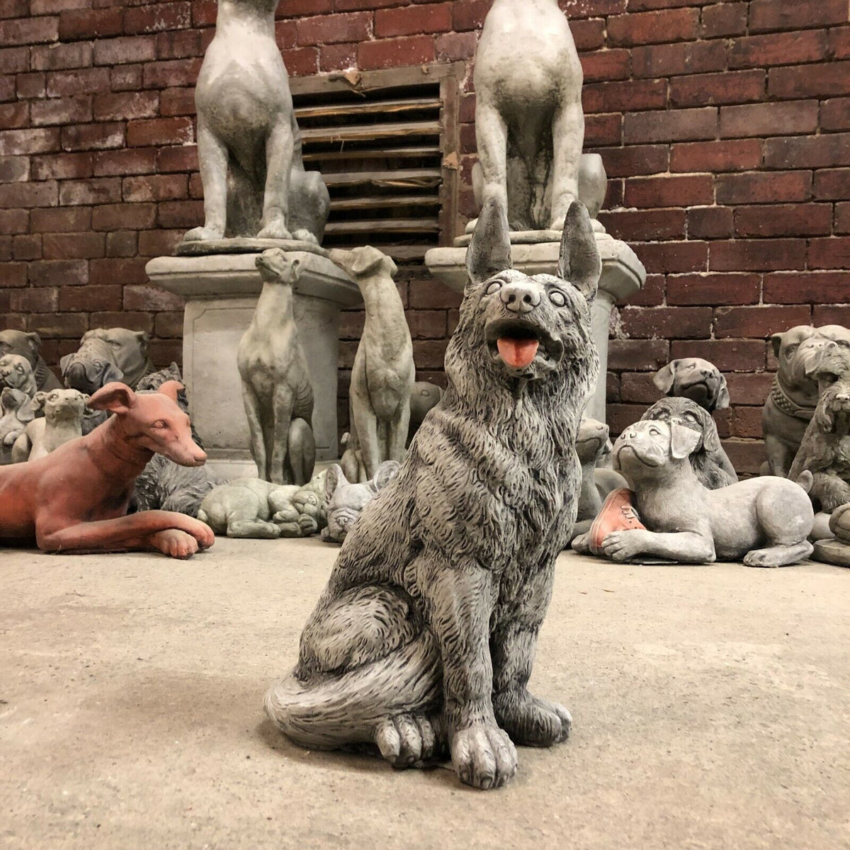 Alsatian Dog Stone Statue placed among other garden sculptures, perfect for enhancing outdoor spaces with a loyal pet-themed ornament.