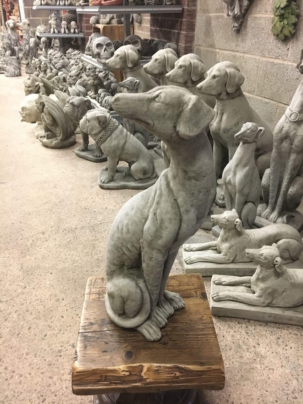 Seated greyhound statue on wooden base surrounded by other dog sculptures, made from solid limestone for outdoor decor.