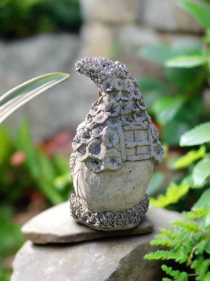 Back view of Stone Fairy Cottage garden ornament showing detailed window and floral textures, set on a rock in a lush garden. Made from solid stone.