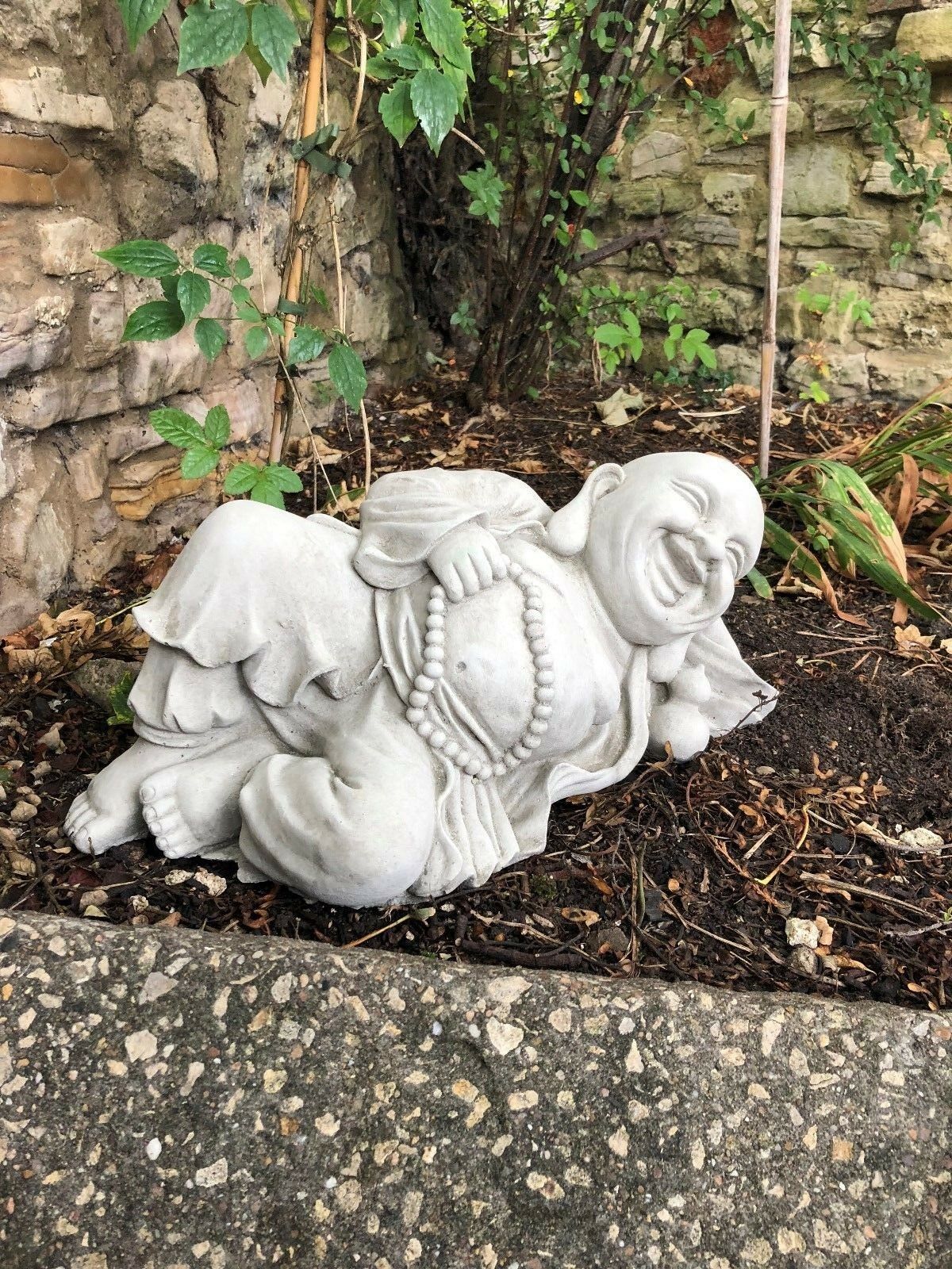 Jolly Stone Buddha Ornament in antique grey finish, reclining with prayer beads, ideal for garden tranquility and outdoor decor.