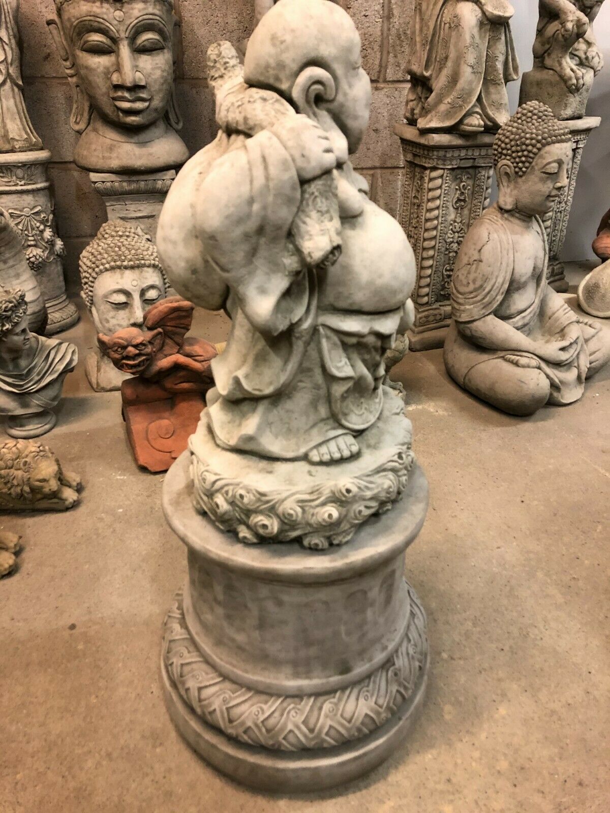 Side view of Laughing Buddha Statue on stone plinth, highlighting intricate robe details and travel sack, perfect for garden or patio decoration.