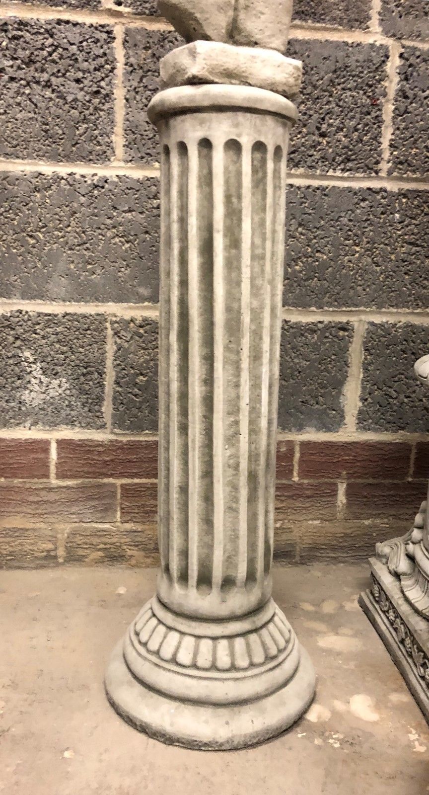 Close-up of a Grecian-style limestone plinth with fluted design and round base. Supports torso statues for elegant garden ornamentation.