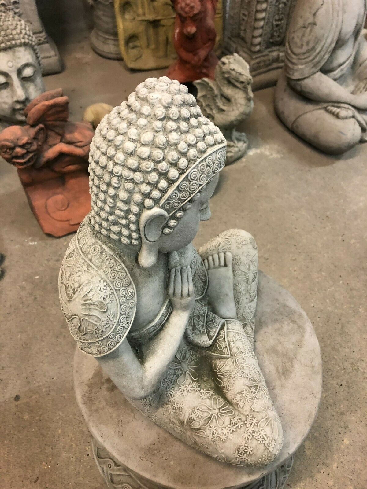 Top view of Stone Buddha Garden Ornament seated cross-legged with hands on cheek. Concrete finish complements modern and traditional garden decor.