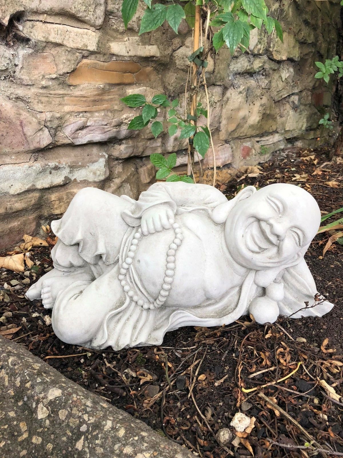 Reclining Jolly Stone Buddha Garden Ornament with joyful expression and detailed robe, perfect for peaceful garden settings.