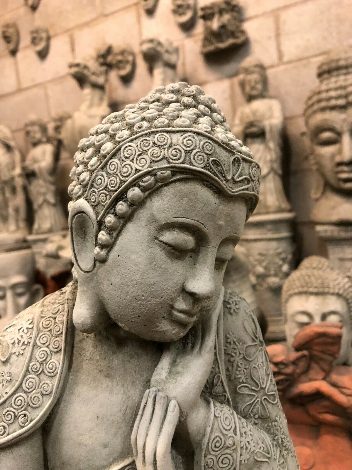 Close-up of Buddha Garden Ornament's peaceful face and textured hair curls. Crafted from durable stone for home and garden meditation spaces.