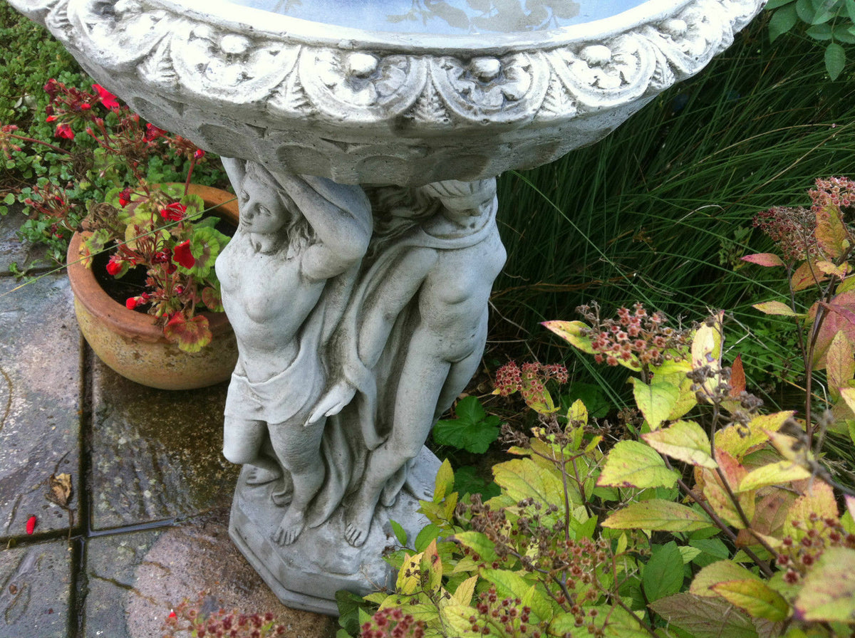 Close-up of Three Graces Bird Bath showing detailed stone carving of classical female figures supporting the deep top bowl.