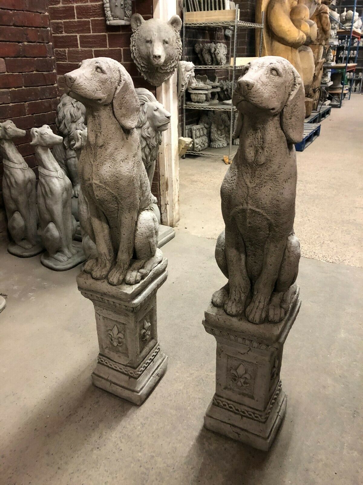 Detailed Stone Hound Dog Garden Statues in antique finish, seated on fleur-de-lis plinths, perfect for lawn ornamentation or entrance decor.