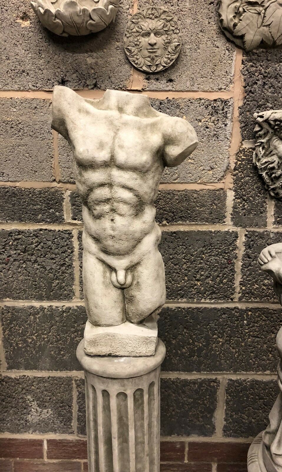 Male torso statue on Grecian plinth with defined musculature and antique grey tone. Weather-resistant stone sculpture for outdoor decor.