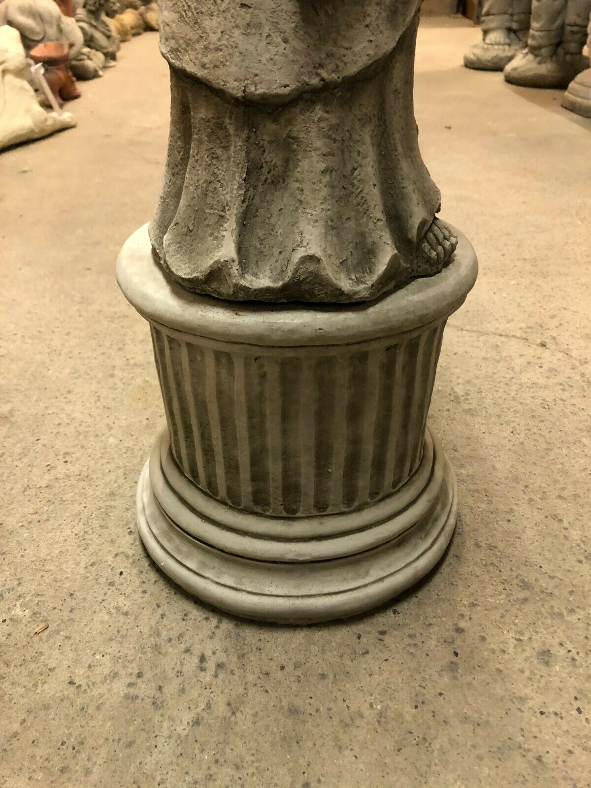 Detailed view of the fluted pedestal base supporting the durable stone Buddha statue for garden display.