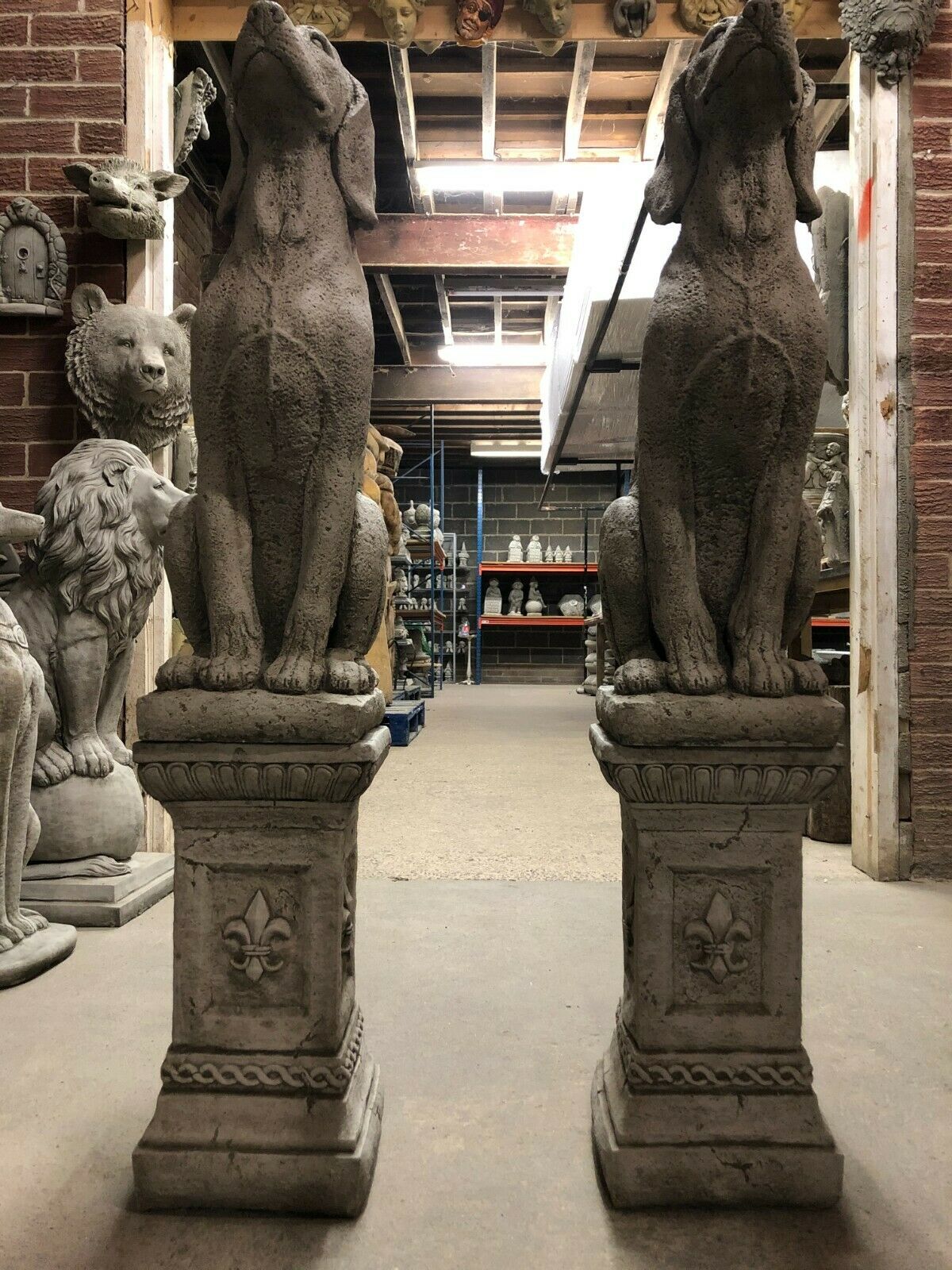 Front view of two solid stone hound statues with antique grey finish, mounted on ornate bases, suitable for garden sculpture displays.