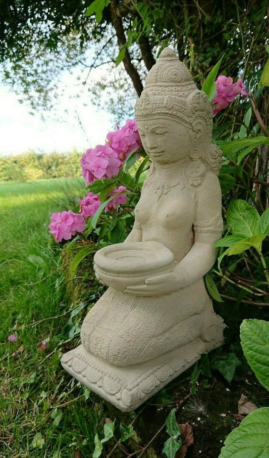 Stone Praying Geisha Garden Statue with intricate detailing and limestone finish, kneeling in a serene garden with pink flowers and greenery.