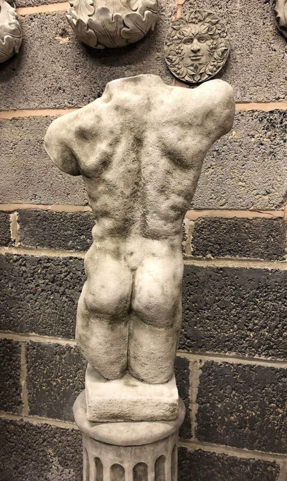 Back of male torso statue on limestone column, showing realistic anatomical detail. Durable and stylish garden ornament.