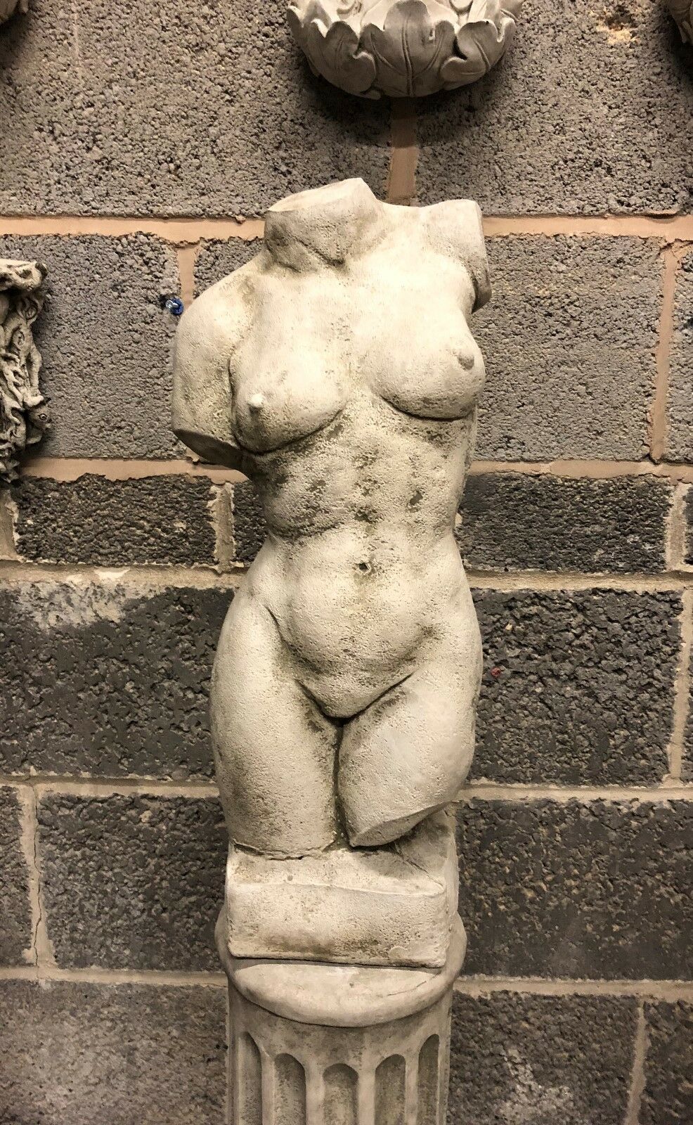 Female torso statue with antique finish on Grecian plinth, featuring detailed curves. Ideal for classical garden or patio decor.