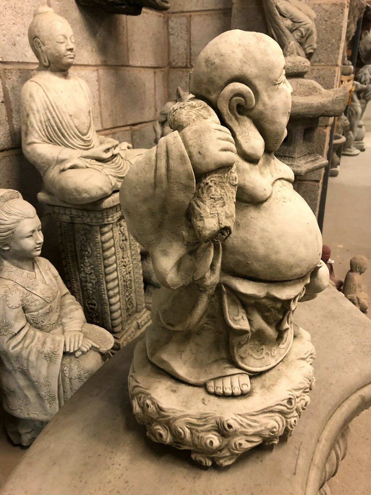 Side view of Stone Laughing Buddha Statue with antique finish, showing sack detail and raised foot, perfect for outdoor Buddhist-themed settings.