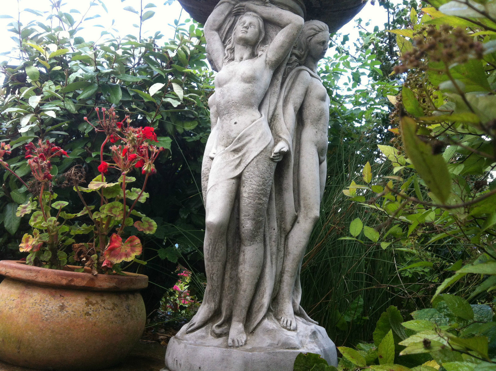 Detailed sculpture of the Three Graces on stone bird bath pedestal, highlighting neoclassical artistry and garden elegance.
