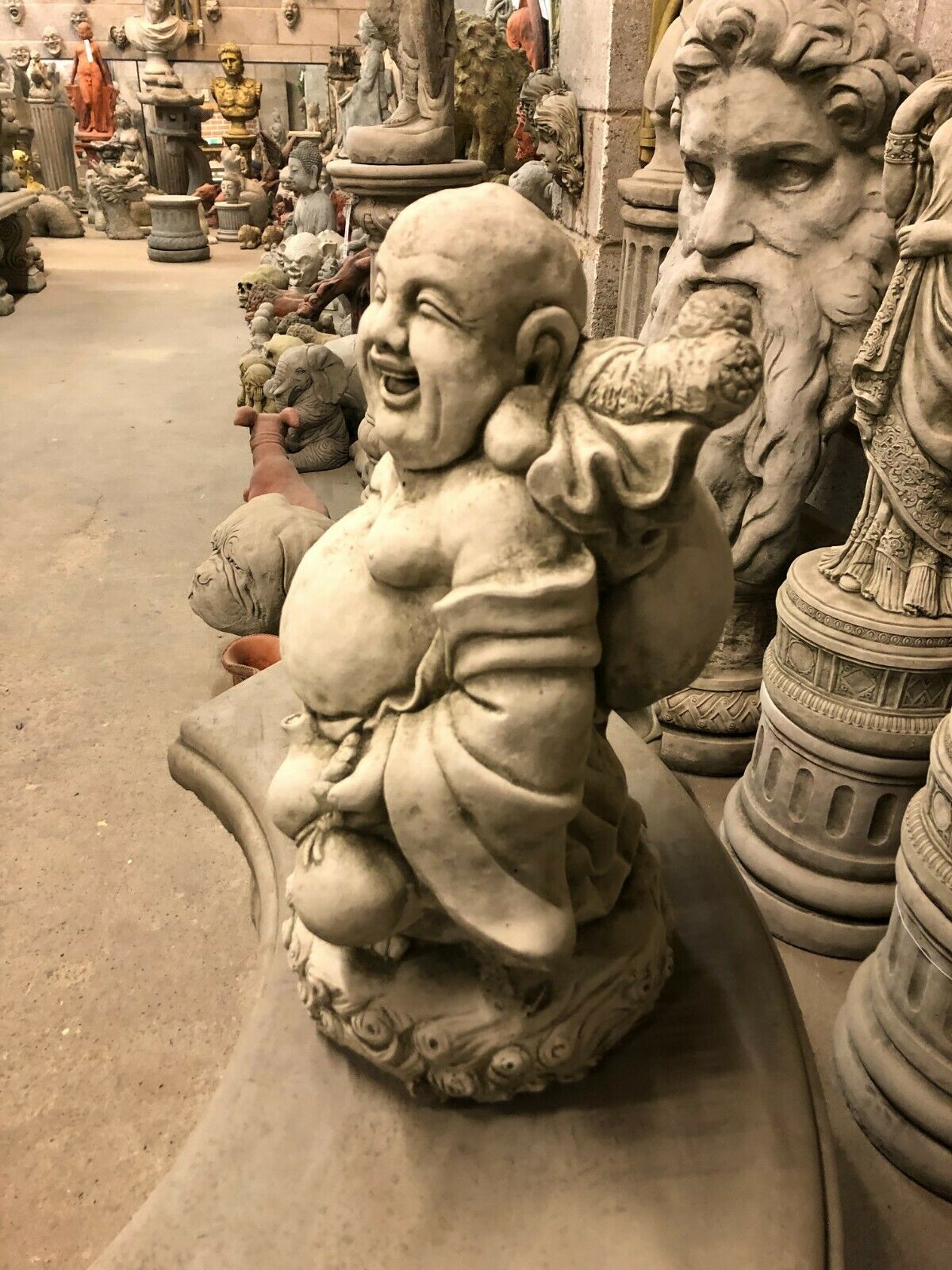 Angled view of Stone Laughing Buddha Statue - Weather Resistant | Antique Finish, highlighting joyful expression and ornate base for garden display.