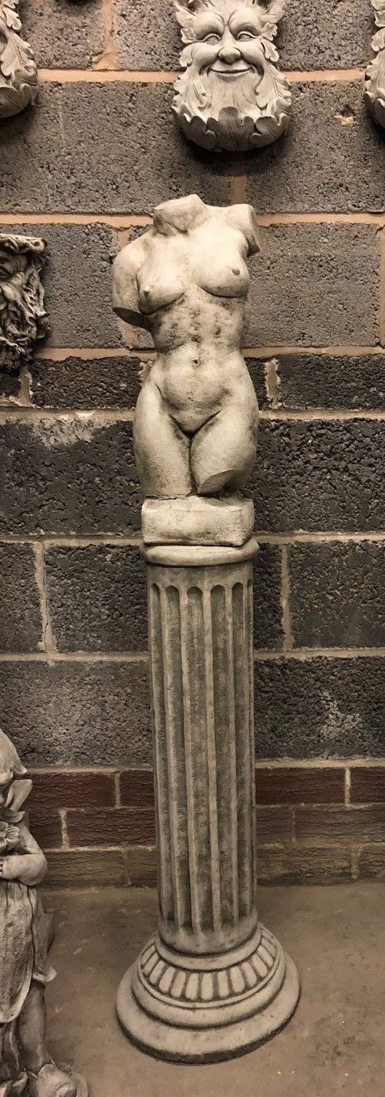Female torso statue on tall Grecian plinth, with detailed stone carving and antique look. Elegant outdoor sculpture for garden decor.
