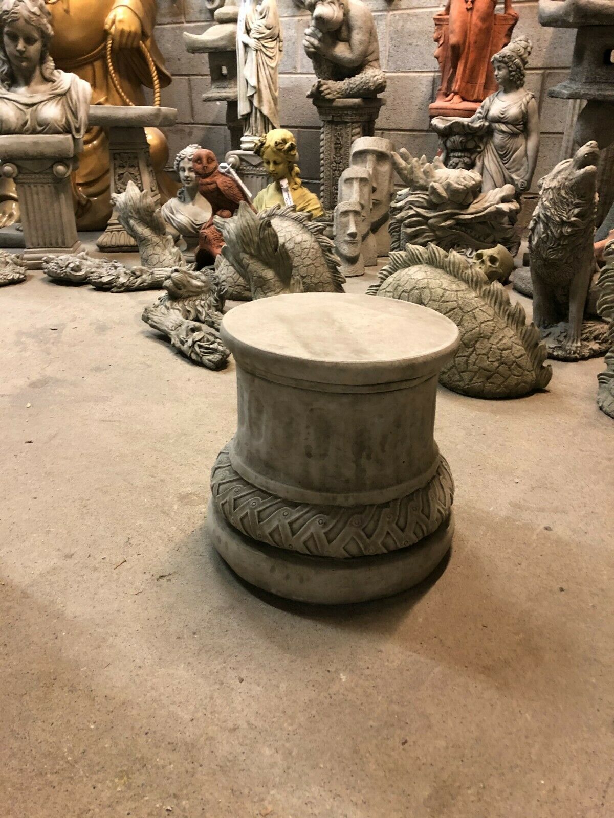 Antique-style solid stone garden plinth placed among various sculptures, highlighting its decorative and durable outdoor use.