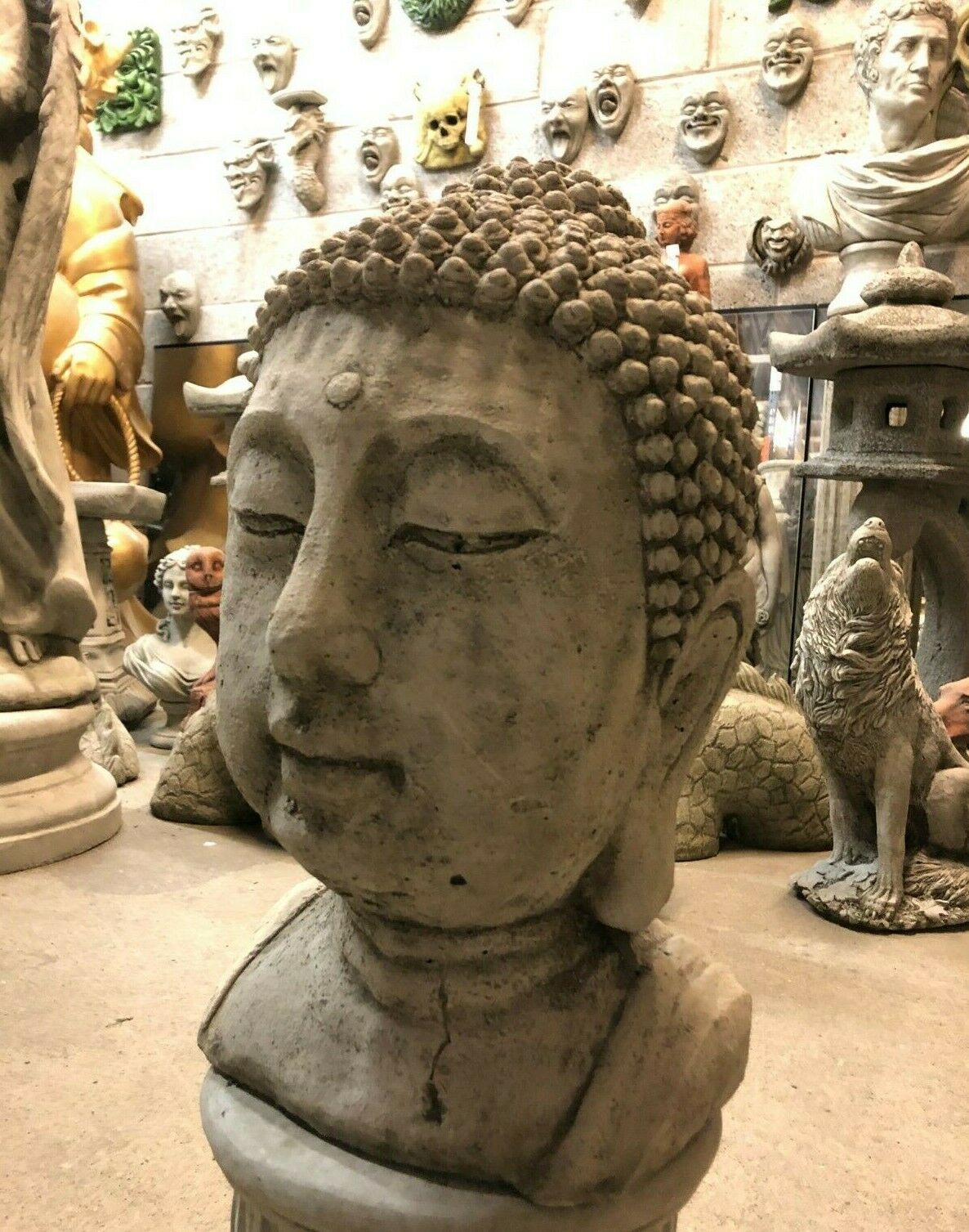 Angled view of Buddha head garden statue made from durable stone. Decorative lawn sculpture with weathered antique texture.