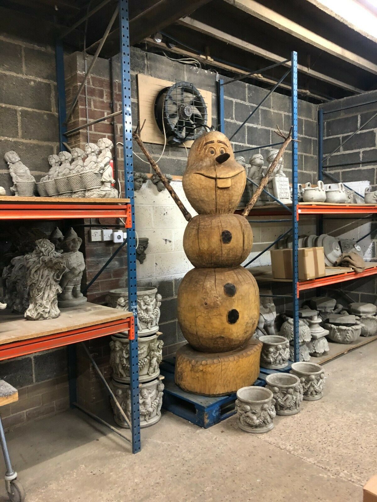 Handcrafted Wooden Olaf Statue - Garden Display standing tall in a workshop, surrounded by stone garden ornaments and sculptures.
